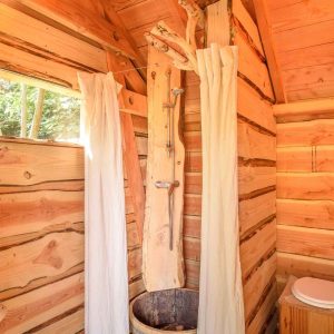 Cabane en bois avec douche en rondins et vue sur la nature environnante.