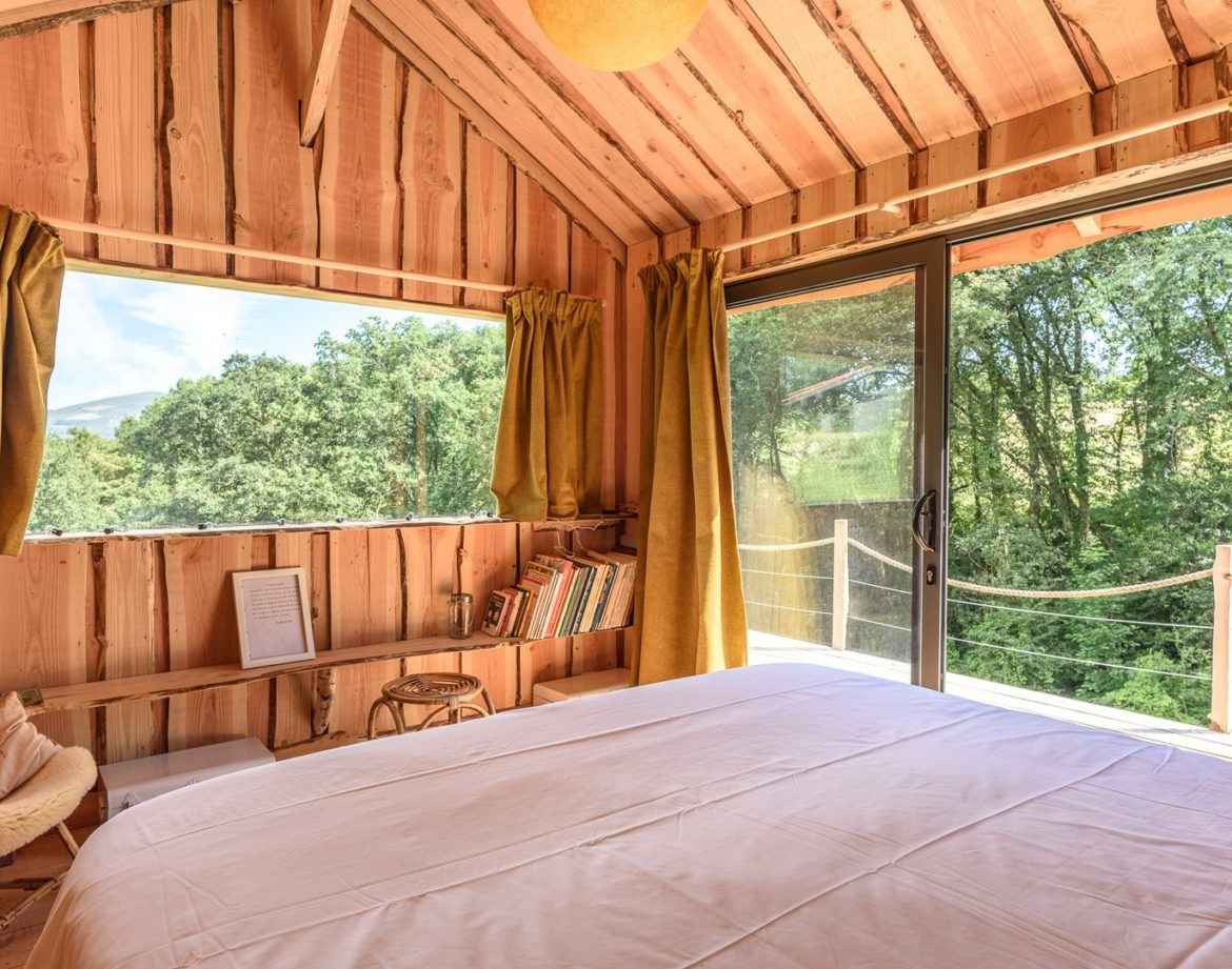 Cabane en bois avec vue sur la nature, lit confortable et lumière naturelle.