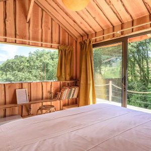 Cabane en bois avec vue sur la nature, lit confortable et lumière naturelle.