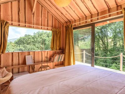 Cabane en bois avec vue sur la nature, lit confortable et lumière naturelle.
