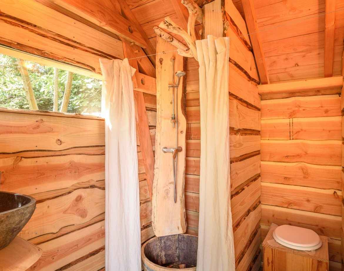 Cabane en bois avec douche en rondins et vue sur la nature environnante.
