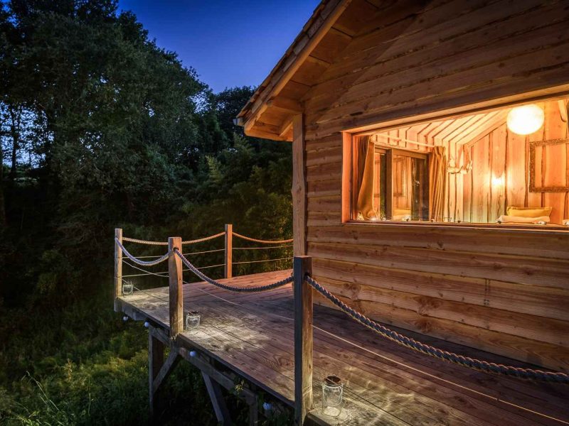 Cabane perchée en bois avec terrasse lumineuse, entourée de verdure en Aquitaine.