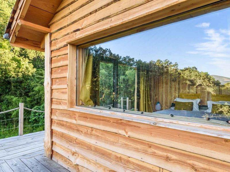 Cabane en bois avec grande fenêtre offrant une vue sur la nature environnante.