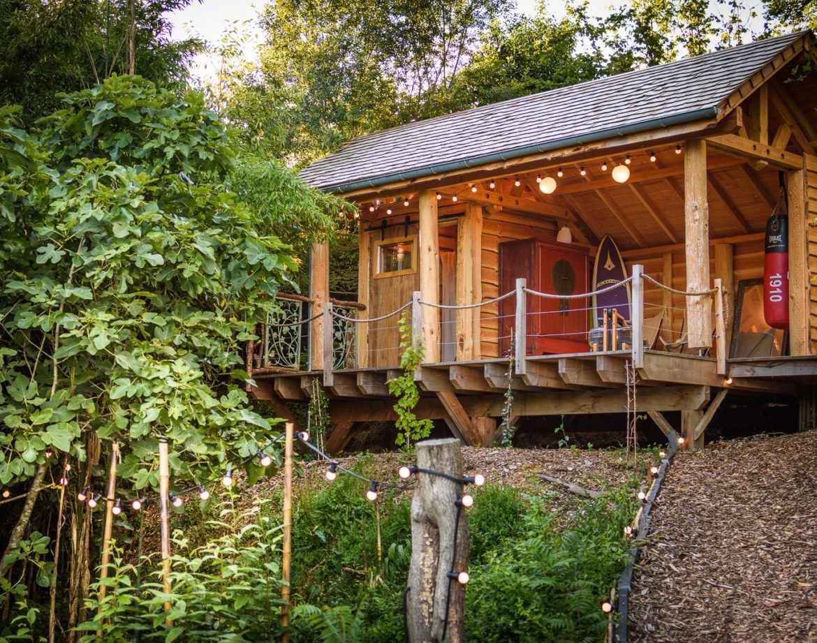 Cabane en bois dans la nature, éclairée par des guirlandes lumineuses.