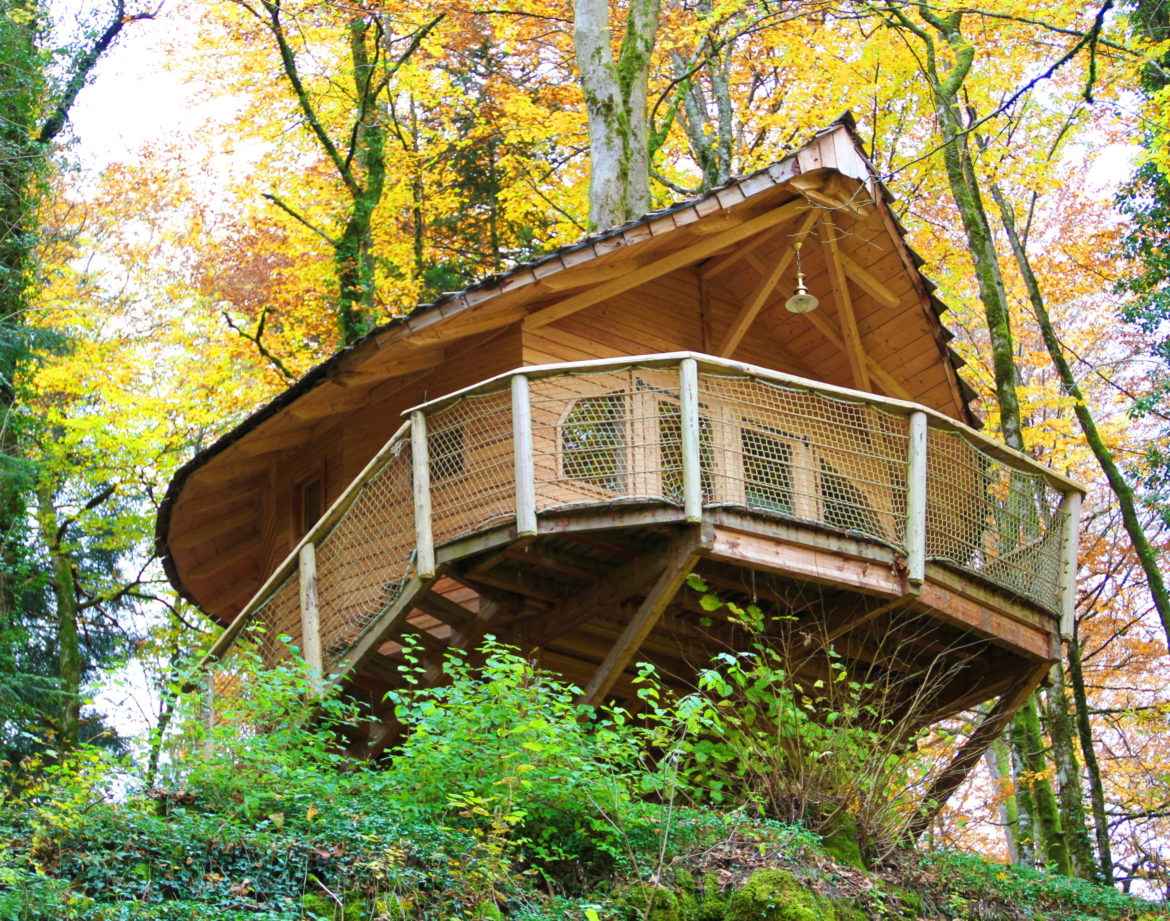 Cabane perchée en bois, entourée de feuillage automnal en Bourgogne-Franche-Comté.