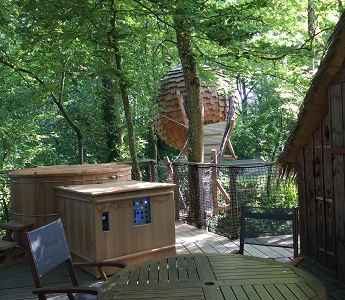 Cabane perchée dans les arbres, entourée de verdure, avec jacuzzi en bois.
