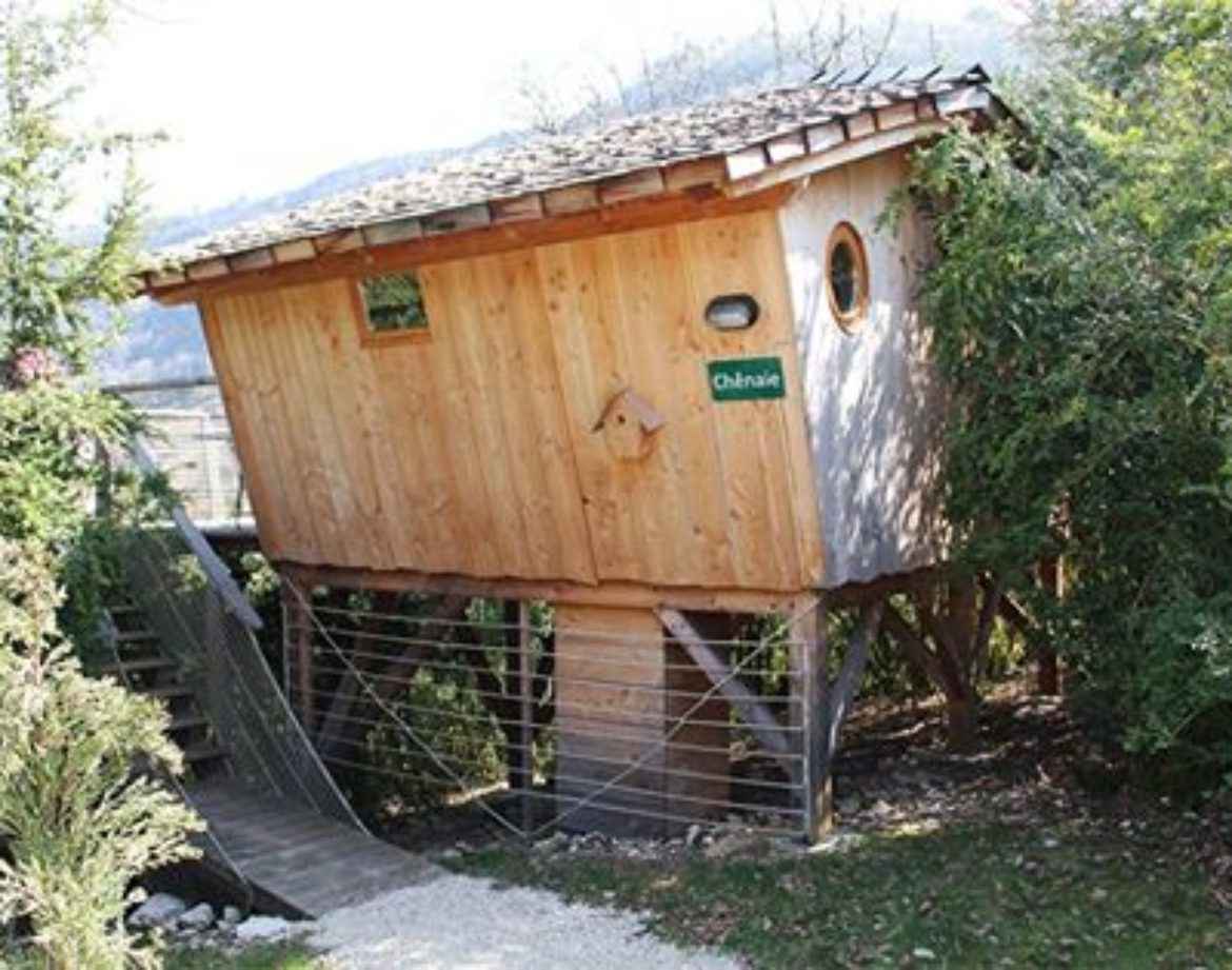 Cabane perchée en bois, entourée de verdure, offrant une vue imprenable sur la nature.