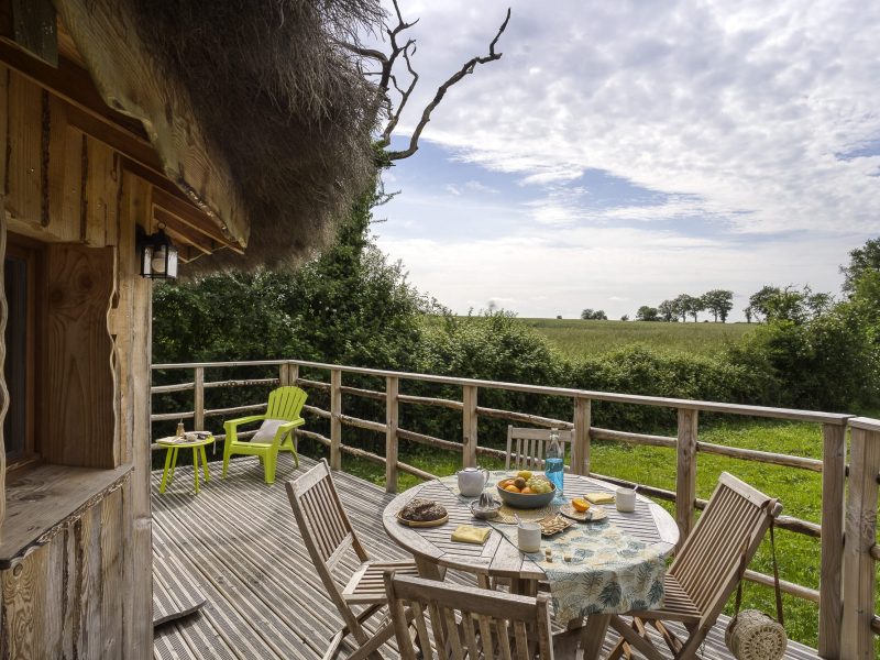 Cabane perchée en bois avec terrasse, vue sur la nature verdoyante.