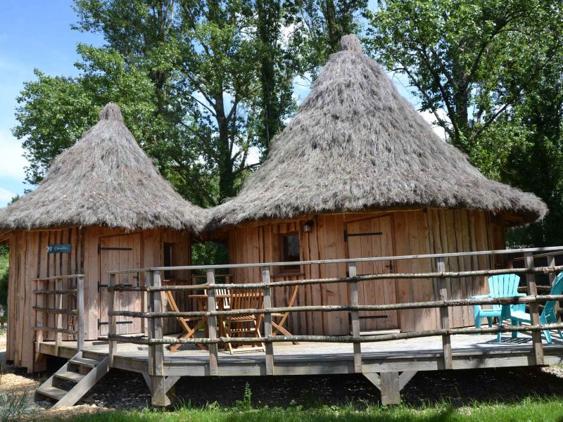 Hébergement en cabanes en bois avec toits de chaume et terrasse en bois.