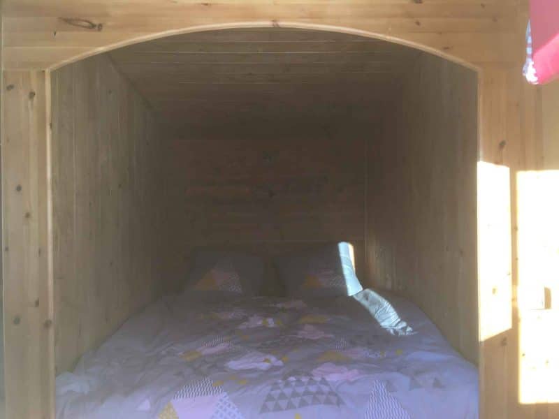 Cabane en bois avec un lit douillet et des draps colorés.