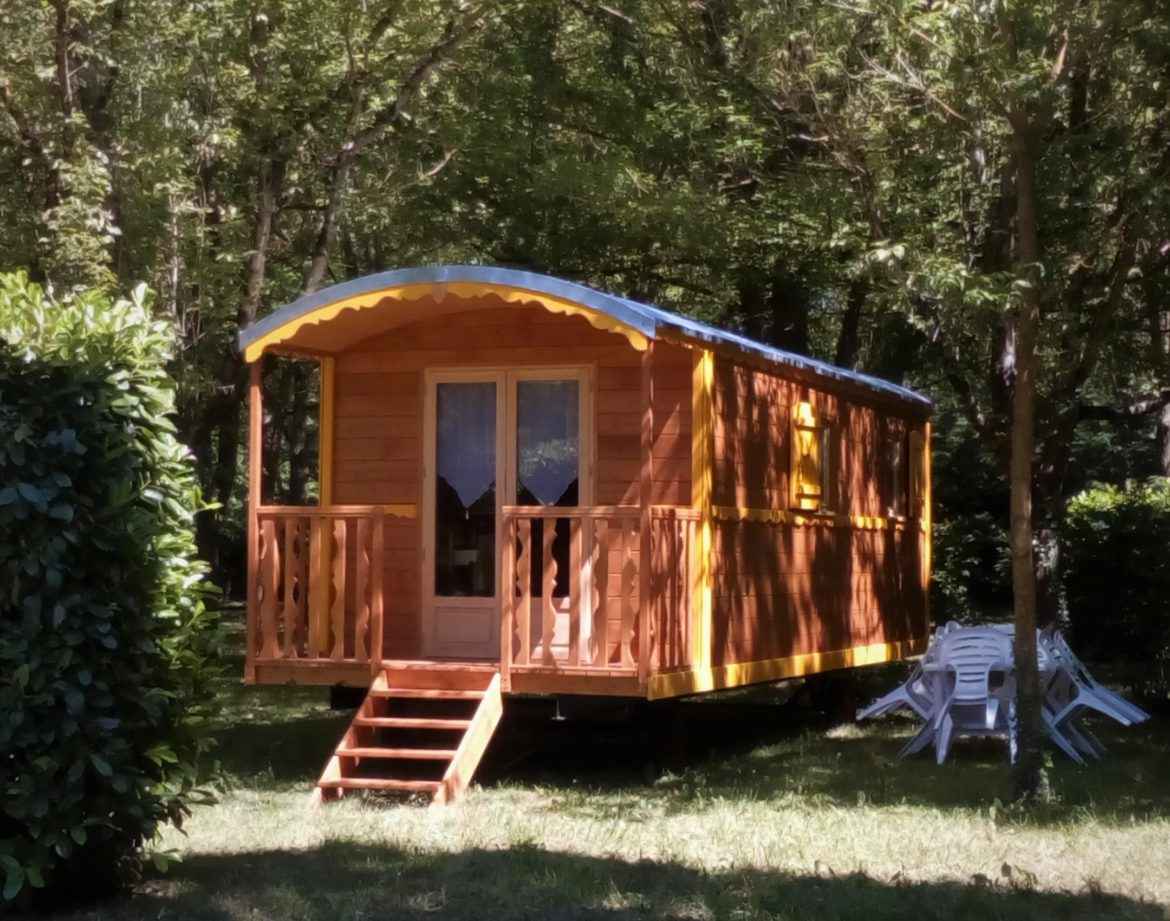 Cabane en bois colorée, entourée darbres, avec terrasse ensoleillée.