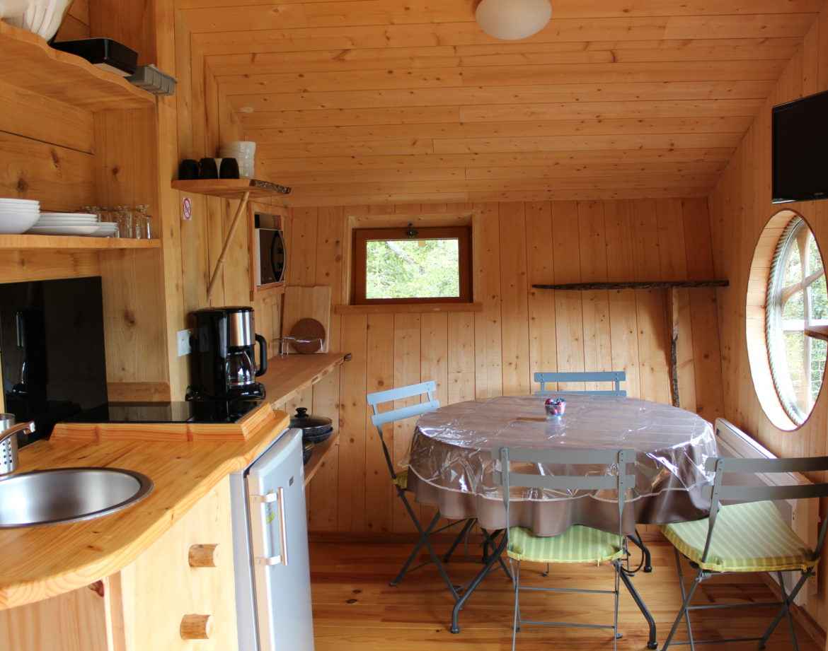 Cabane en bois chaleureuse avec cuisine équipée et table ronde lumineuse.