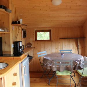 Cabane en bois chaleureuse avec cuisine équipée et table ronde lumineuse.
