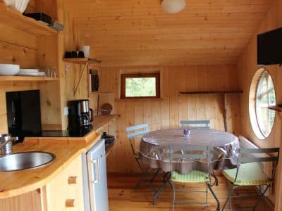 Cabane en bois chaleureuse avec cuisine équipée et table ronde lumineuse.
