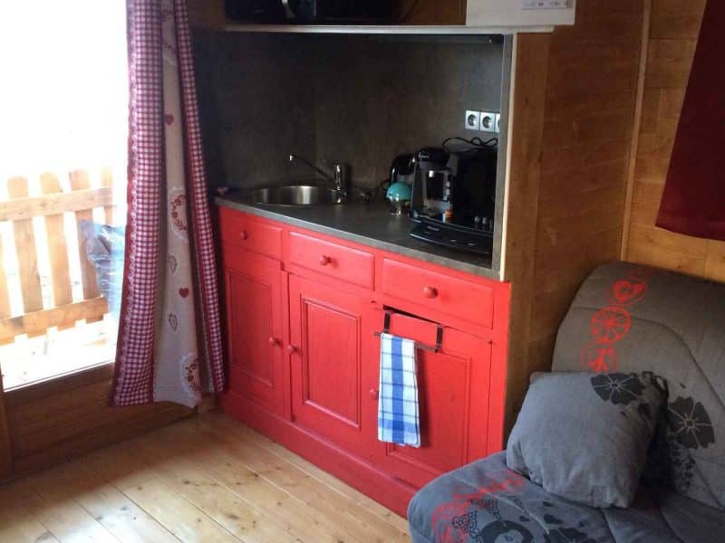 Chalet cosy avec cuisine rouge et coin salon confortable en bois.