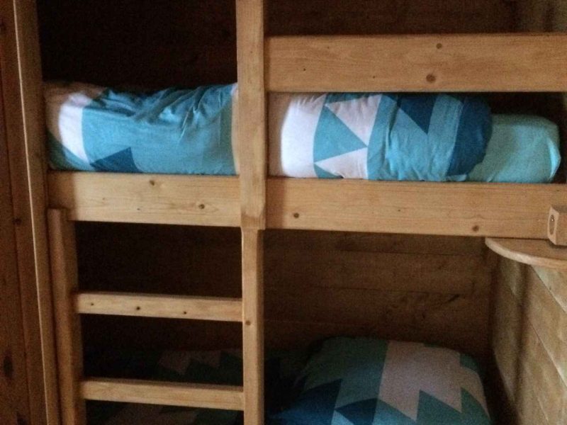 Chalet en bois avec lits superposés et draps aux motifs géométriques bleus.