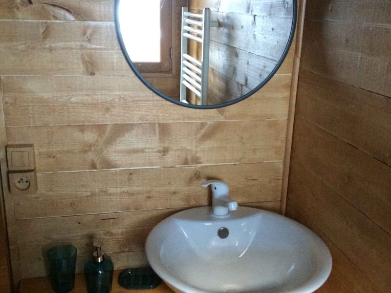 Salle de bain en bois avec lavabo rond et miroir décoratif. Ambiance chaleureuse.