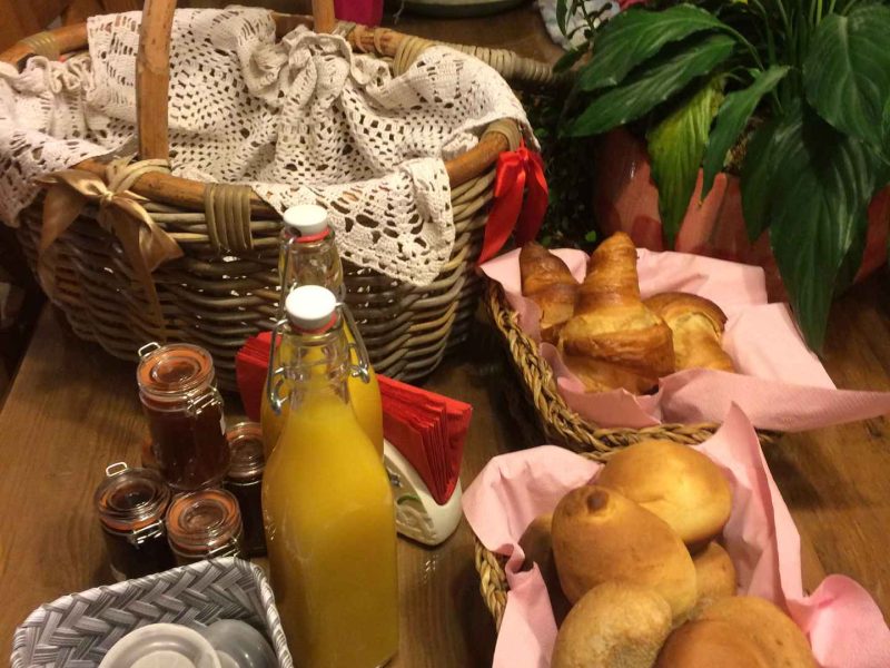 Gîte accueillant avec panier de pains frais et jus dorange sur une table en bois.