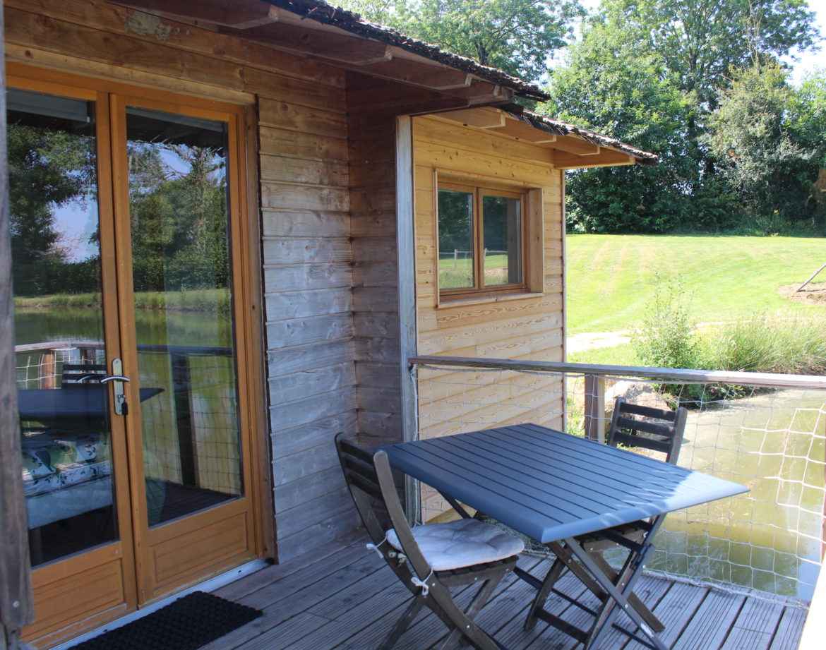 Cabane sur pilotis en bois avec terrasse, vue sur un paisible étang.