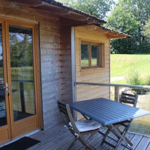 Cabane sur pilotis en bois avec terrasse, vue sur un paisible étang.