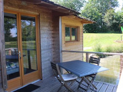 Cabane sur pilotis en bois avec terrasse, vue sur un paisible étang.