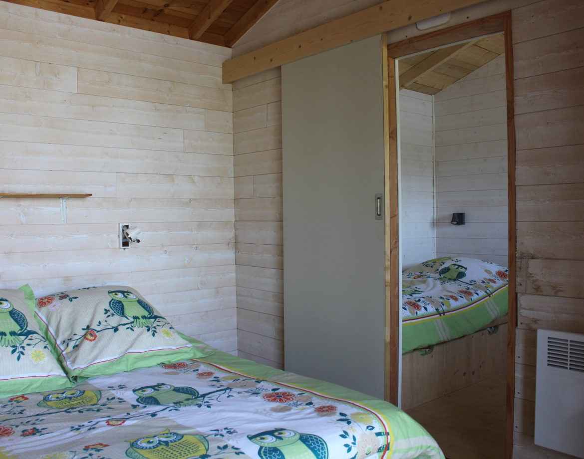 Chalet en bois avec lit décoré de hiboux et murs clairs, ambiance cosy.