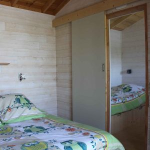 Chalet en bois avec lit décoré de hiboux et murs clairs, ambiance cosy.