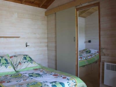 Chalet en bois avec lit décoré de hiboux et murs clairs, ambiance cosy.
