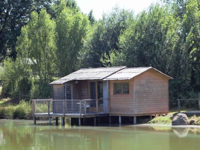 Cabane en bois sur pilotis au bord dun étang, entourée de verdure luxuriante.