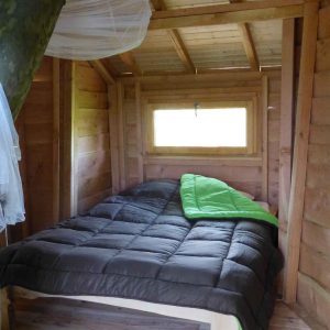 Cabane en bois dans un arbre, lit confortable avec couette verte et murs en bois.