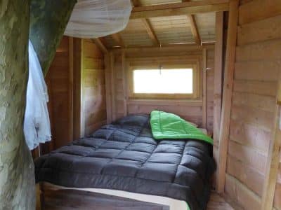 Cabane en bois dans un arbre, lit confortable avec couette verte et murs en bois.