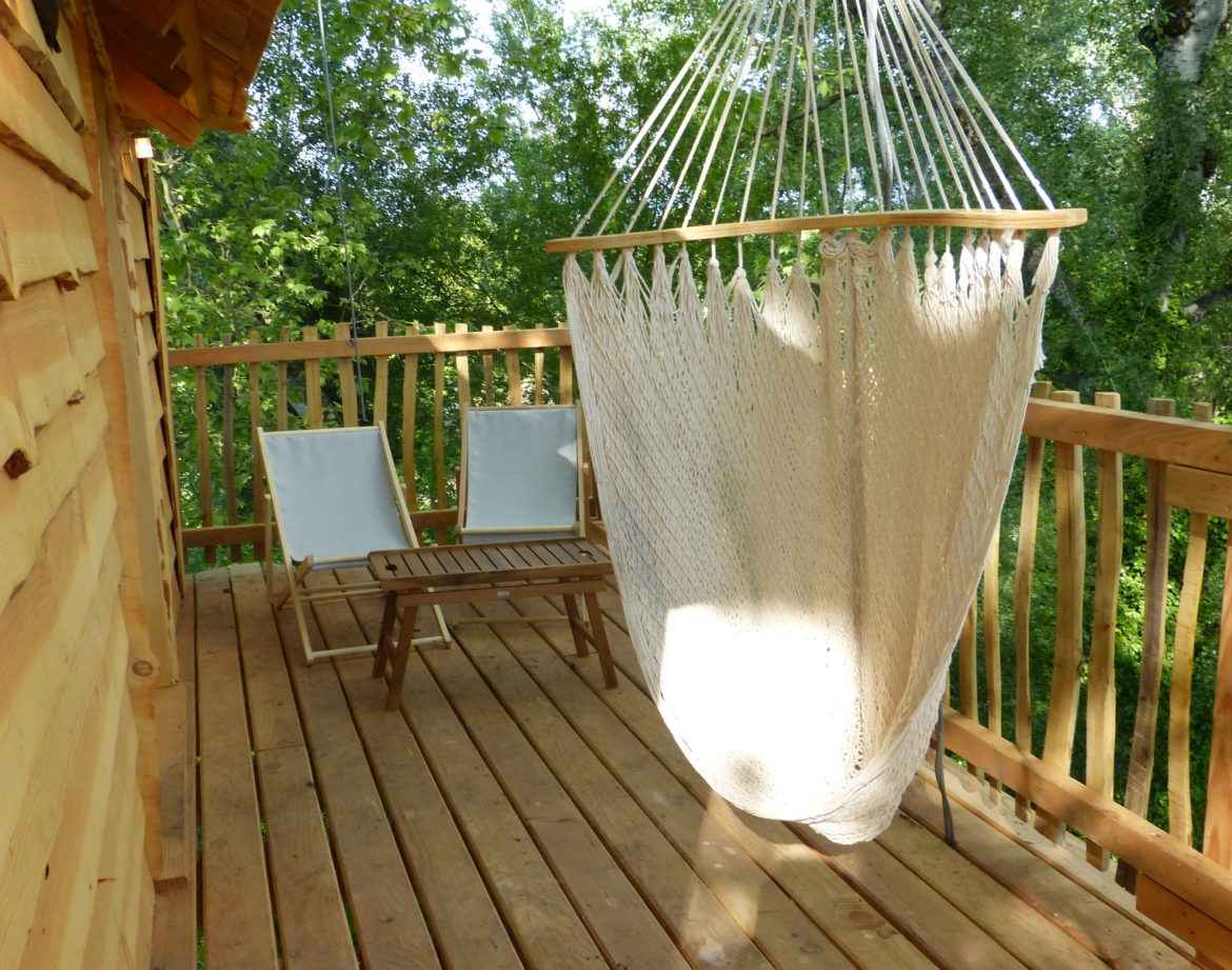 Cabane perchée en bois avec hamac suspendu et chaises sur la terrasse.