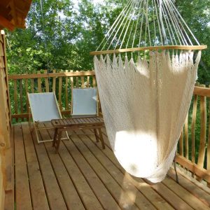 Cabane perchée en bois avec hamac suspendu et chaises sur la terrasse.