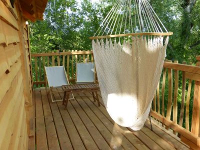 Cabane perchée en bois avec hamac suspendu et chaises sur la terrasse.