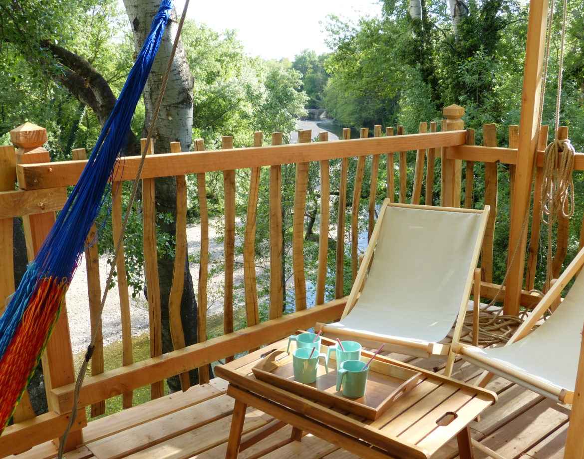 Cabane perchée en bois avec hamac et vue sur la rivière, idéale pour se détendre.