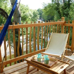 Cabane perchée en bois avec hamac et vue sur la rivière, idéale pour se détendre.