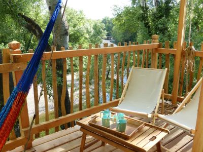 Cabane perchée en bois avec hamac et vue sur la rivière, idéale pour se détendre.