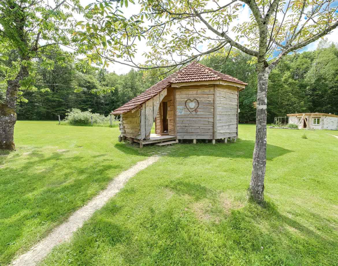 Cabane en bois ronde, entourée de verdure, avec un chemin menant à lentrée.