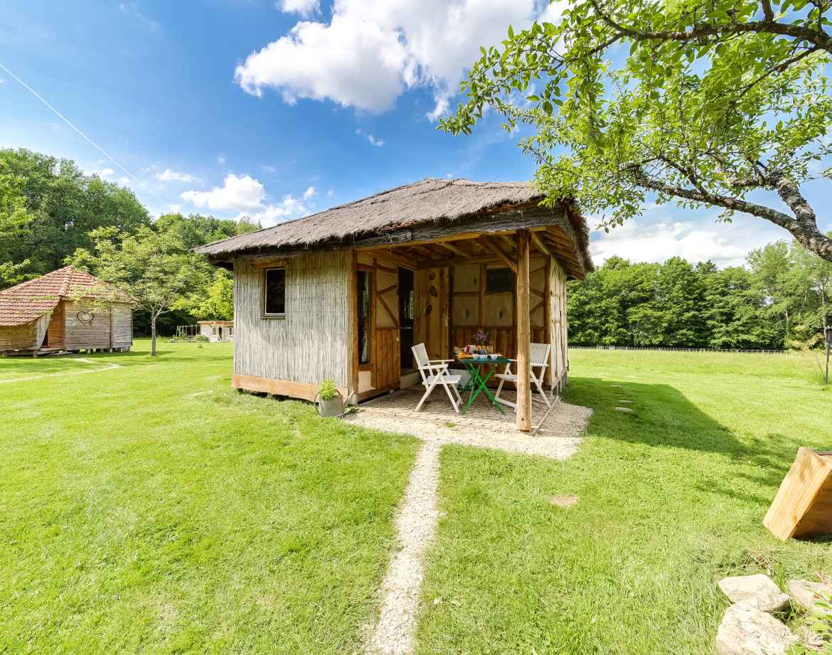 Cabane en bois avec toit de chaume, entourée de verdure et dun jardin accueillant.