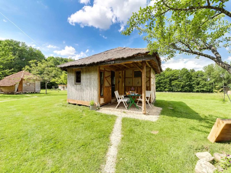 Cabane en bois avec toit de chaume, entourée de verdure et dun jardin accueillant.