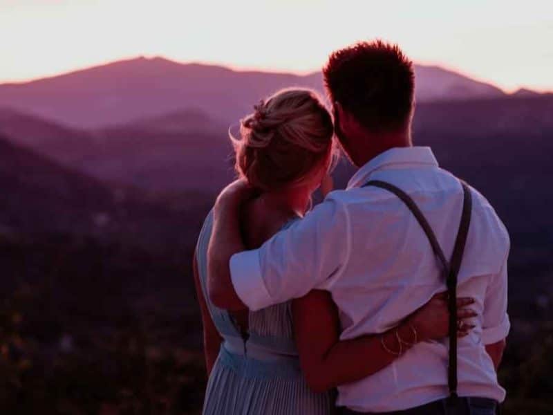Couple romantique admirant le coucher de soleil depuis un chalet en montagne.