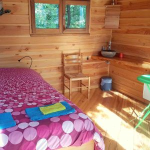 Chalet en bois avec lit douillet, décoré de couleurs vives et lumière naturelle.