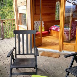 Cabane en bois avec terrasse, fauteuils noirs et vue sur la nature environnante.