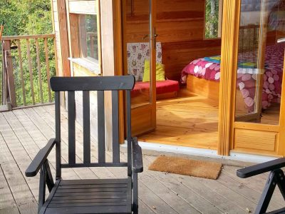 Cabane en bois avec terrasse, fauteuils noirs et vue sur la nature environnante.
