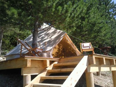 Tente glamping sur plateforme en bois, entourée de pins en Auvergne-Rhône-Alpes.