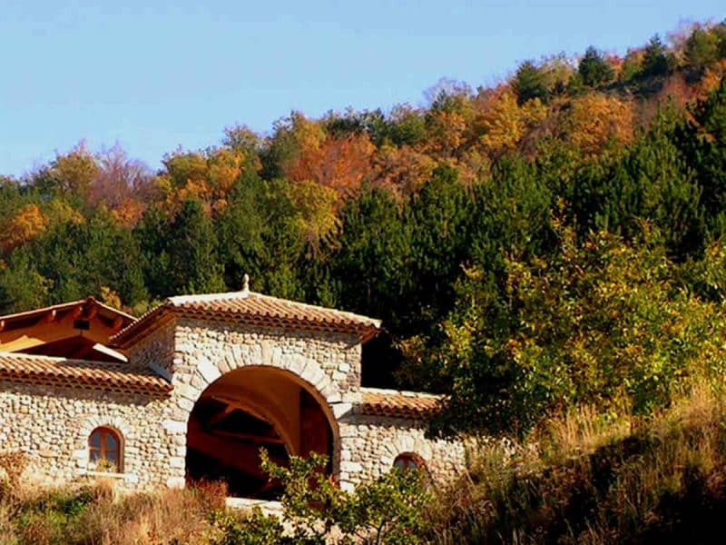 Gîte en pierre avec un arc, niché au milieu dune forêt colorée dautomne.