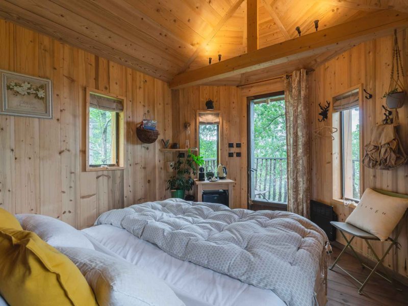 Cabane en bois cosy avec lit douillet et vue sur la nature environnante.