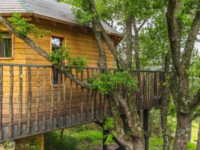 Cabane perchée en bois, entourée darbres, avec une terrasse en bois.