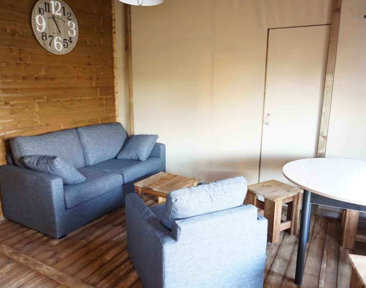 Hébergement insolite en bois avec salon cosy et horloge murale moderne.