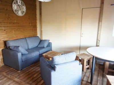 Hébergement insolite en bois avec salon cosy et horloge murale moderne.
